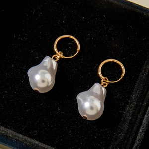 Close-up of golden hoop earrings with irregular Baroque pearls on a black velvet box