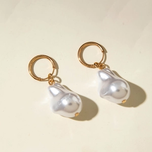 Detail of baroque pearl drop earrings with polished gold metal hoops on white surface