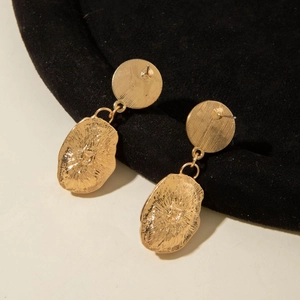 Close-up of golden baroque style earrings with hammered texture on black velvet