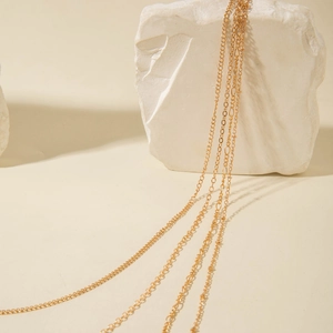 Elegant multi-layered gold plated necklace chains displayed on a white marble pedestal