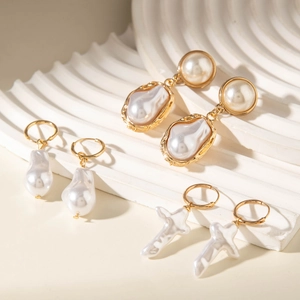 Three pairs of elegant Baroque pearl earrings in gold settings on a white geometric stand