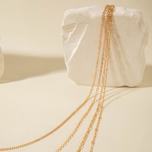 Minimalist multi-layered gold chains draped over stone showing various linked patterns