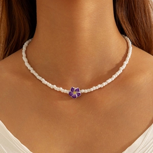 Detail of white beaded necklace featuring a purple resin flower pendant for summer beach style