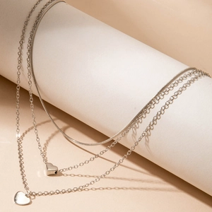 Detail of layered silver necklaces with heart pendants draped over a beige cylinder
