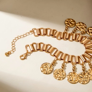 Detail of a vintage gold anklet featuring textured coin charms and a tassel leaf design