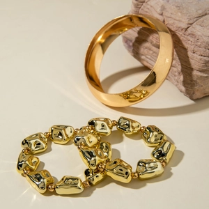Détail de manchette dorée épaisse et bracelets perlés irréguliers sur fond de pierre neutre