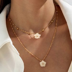 Detail of layered gold chain necklaces featuring white flower pendants on a model