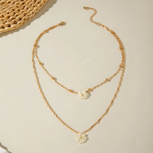 Detail of layered gold chain necklace with white floral pendants and lobster clasp