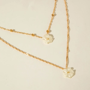 Detail of layered gold chain necklace featuring delicate white resin flower pendants