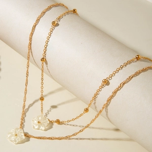 Detail of layered gold chain necklace featuring delicate white shell flower pendants