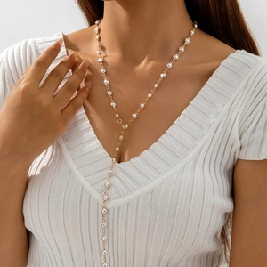 Close-up of a layered golden Y-necklace with small white pearls on a model wearing V-neck