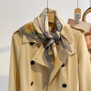 Silk-like fashion scarf with chain print and yellow sun motif tied on a beige trench coat