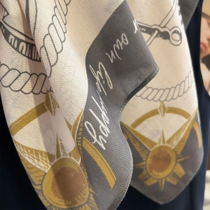 Close-up of silk scarf showing detailed nautical rope patterns and golden sun emblems