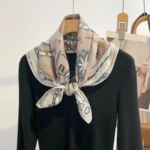 Elegant chain print silk scarf in beige and tan draped over a black knit top