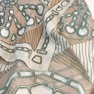 Detailed close-up of chain print silk scarf fabric with elegant beige and brown patterns