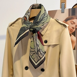 Silk-like floral leaf print square scarf styled on a beige trench coat collar