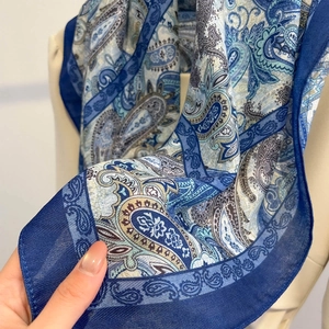 Detailed close-up of blue paisley pattern scarf with silky texture and solid border