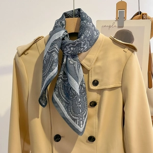 Bandana classique bleu à motif paisley noué avec élégance sur un trench-coat beige chic