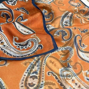 Detail of vibrant orange cotton paisley scarf featuring intricate navy stitched edges