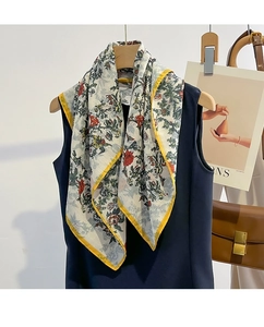 Detailed shot of a floral silk scarf with yellow borders on a wooden hanger with a top