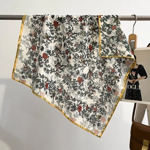 Floral print silk square scarf with yellow borders hanging in a stylish lifestyle setting