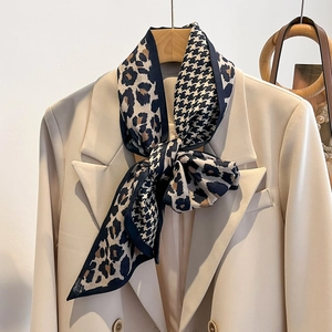 Détail d'un foulard en soie léopard et pied-de-poule noué sur un blazer beige chic