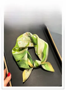 Vue détaillée d'un foulard en soie à fleurs vert et jaune sur un plateau noir élégant