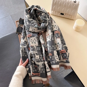 Détail d'une écharpe grise à motif chat avec pompons à côté d'un sac blanc matelassé