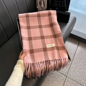 Detail of pink and brown plaid cashmere scarf with soft tassels on a grey sofa