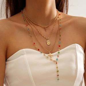 Detail of layered gold necklace with colorful crystals, cross charms and saint medal