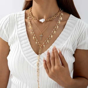 Close-up of layered gold necklace with white pearl and sparkling cross pendants