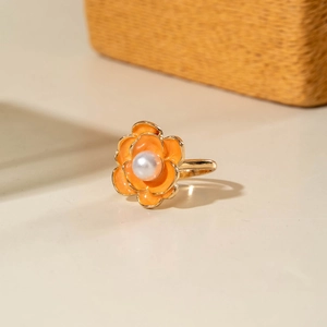Dettaglio di un anello barocco a forma di camelia in smalto arancione con perla bianca