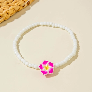 Detail of bohemian white beaded anklet with a pink frangipani flower on sandy background