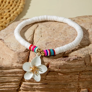 Close-up of Bohemian beaded anklet with white clay flower charm on a natural rock