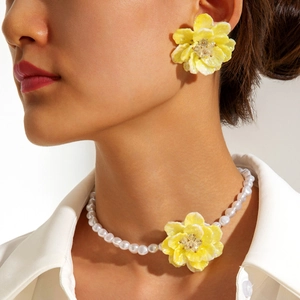 Close-up of vibrant yellow flower earrings and white pearl necklace on a female model