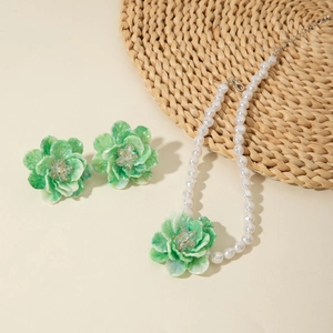 Detail view of a floral jewelry set with green resin petals and white pearl necklace