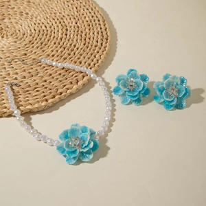 Detail of light blue floral earrings and white resin pearl necklace on woven mat