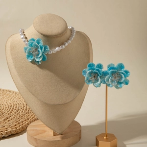 Elegant blue floral jewelry set featuring a pearl necklace and earrings on a stand