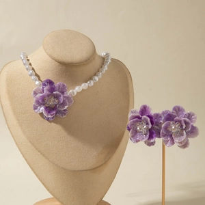 Detailed view of purple floral jewelry set with pearl necklace on a velvet bust display