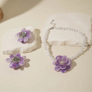 Detail of purple layered flower jewelry set with white pearl necklace on stone props