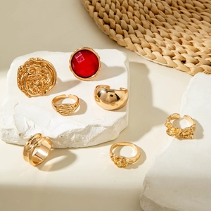 Detail of 7-piece gold metal ring set with red gemstone on textured stone surface