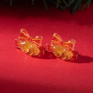 Detail of Christmas stud earrings featuring red bows and golden bells on a festive background