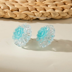 Macro detail of sky blue resin flower earrings with glitter and silver studs on ivory surface