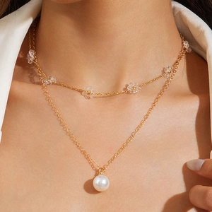 Dettaglio di collana dorata a strati con petali di cristallo e pendente a perla