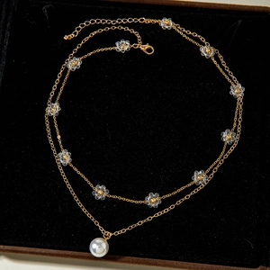 Dettaglio di collana dorata a strati con pendente di perla e fiori in acrilico