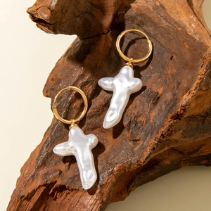 Vue détaillée de créoles dorées avec pendentifs croix en perle baroque sur support en bois