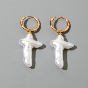 Détail de créoles dorées avec croix en perles baroques sur fond gris neutre