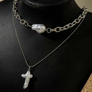 Gros plan d'un collier multicouche argenté avec perle baroque et pendentif croix