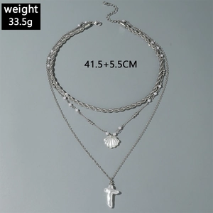 Détail d'un collier multi-rangs argenté avec pendentif coquillage et croix en perle