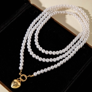 Detalle de collar de perlas de varias capas con colgante de corazón dorado en terciopelo